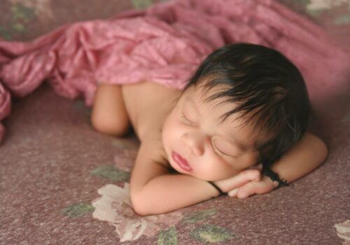 A newborn baby sleeping on a pink blanket.