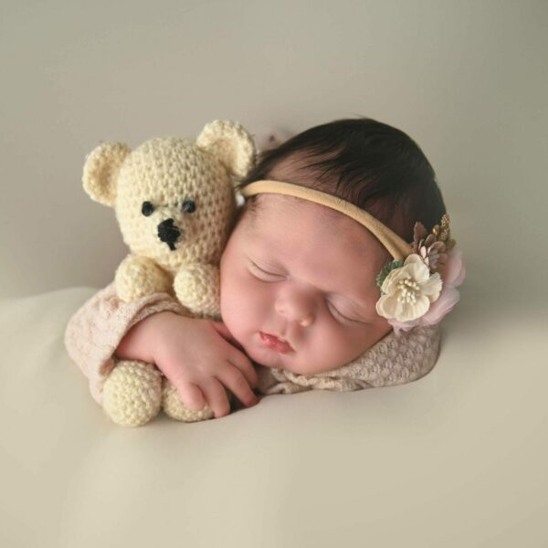 A baby sleeping with a crocheted teddy bear.