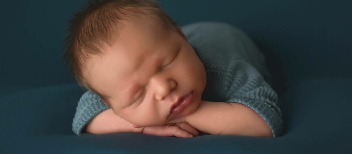 Newborn baby sleeping peacefully in a blue outfit, resting on a soft surface.