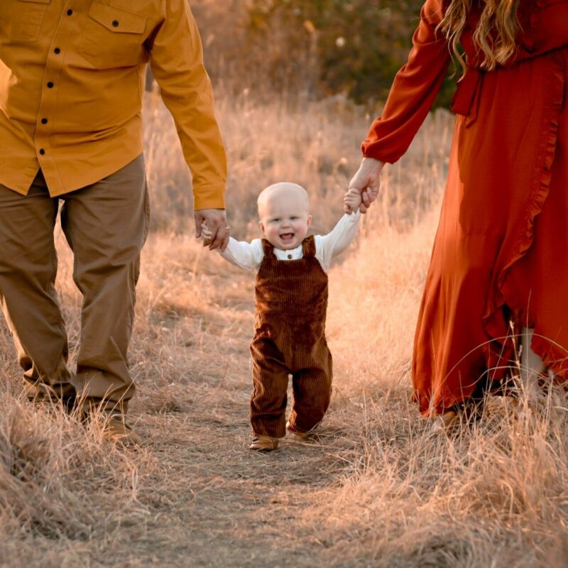 A family holding hands while walking through a field at sunset.