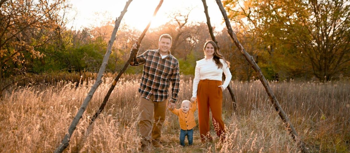 A family is standing in a field with a teepee in the background.