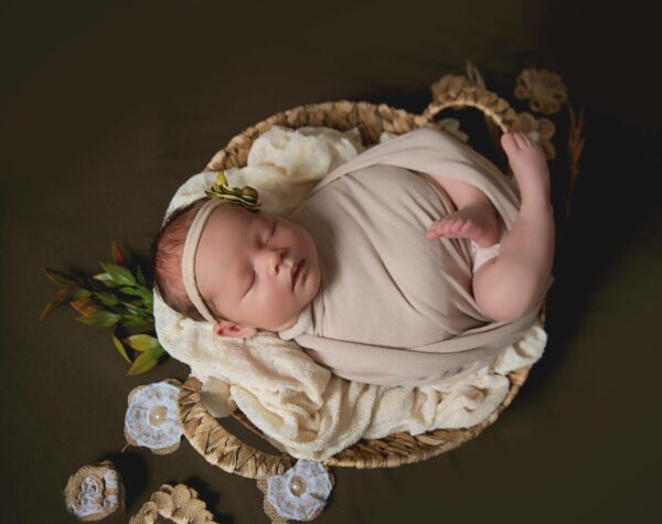 Newborn baby swaddled in cloth, sleeping peacefully in a woven basket with decorative elements, captured during a family photography session in Saint Paul, Minnesota.