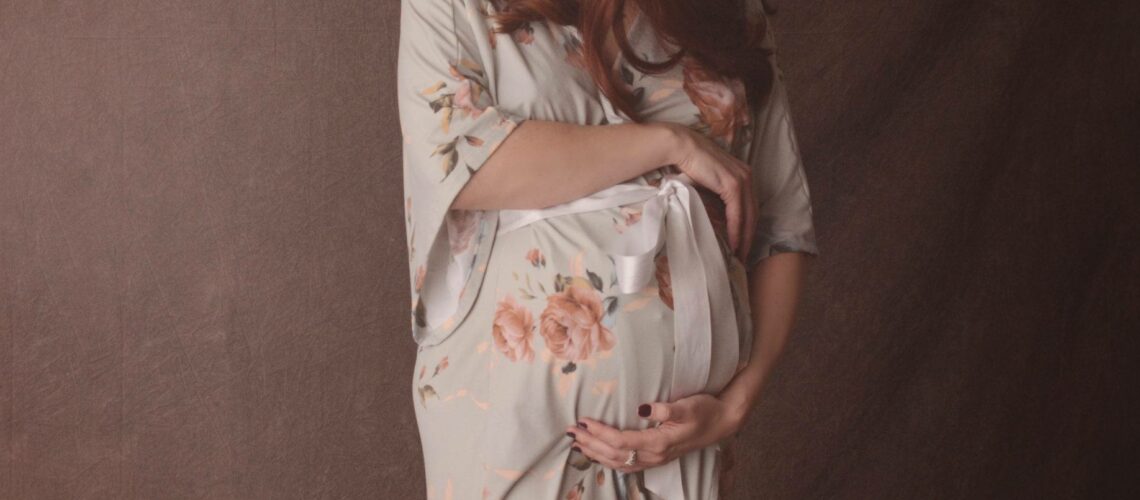A pregnant woman in a floral robe posing for a photo.