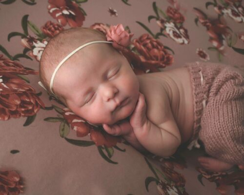 A newborn girl sleeping on a floral blanket.