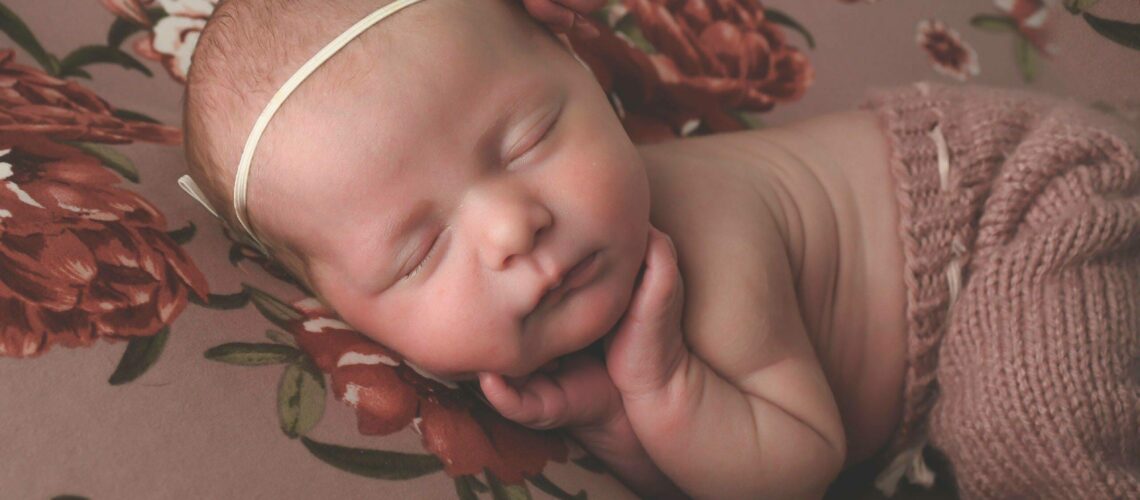 A newborn girl sleeping on a floral blanket.