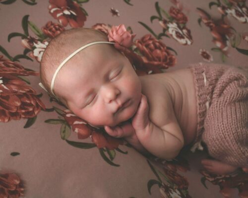 A newborn girl sleeping on a floral blanket.