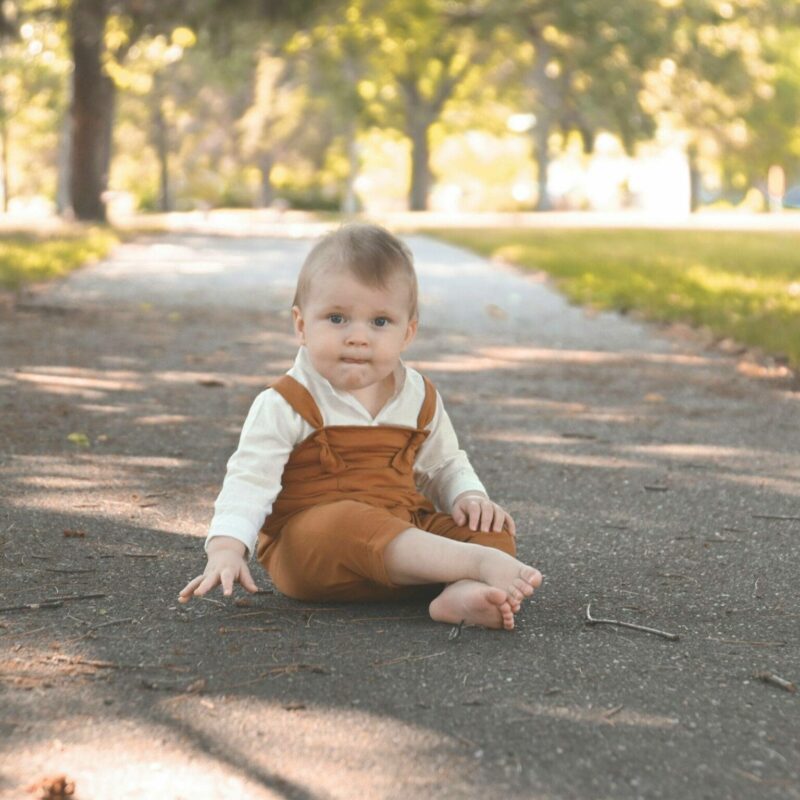 A baby sitting on a path in a park.