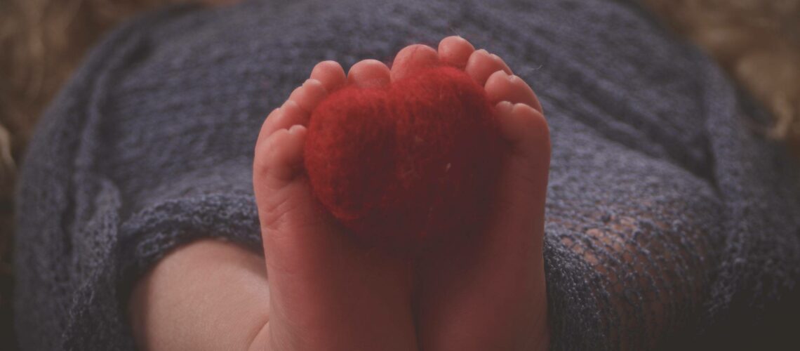 A baby's feet are wrapped in a blanket with a red heart.