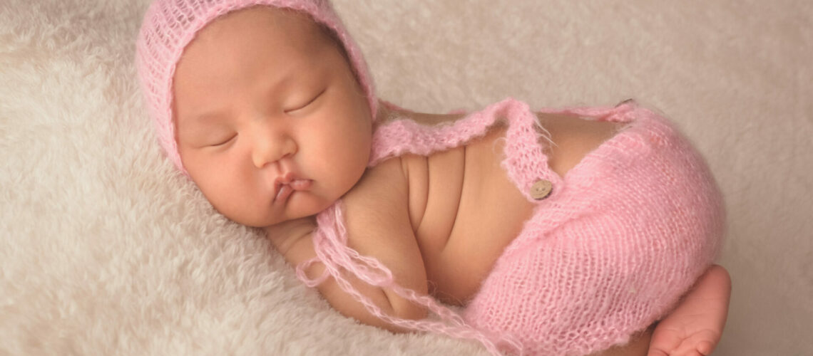 A newborn baby sleeping in a pink knitted outfit.