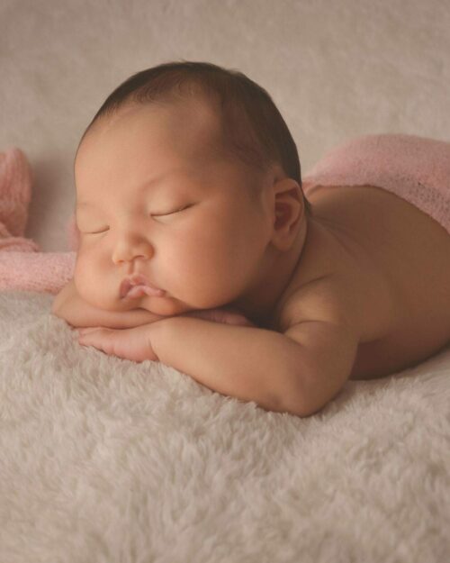 A newborn baby sleeping on a white blanket.