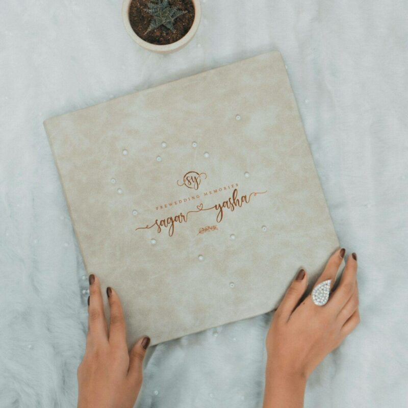 A person holds a textured cover titled "Wedding Memories" on a soft, white surface, next to a small potted cactus.