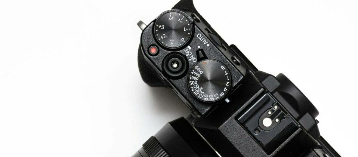 Close-up of a black digital camera on a white background, focusing on the top controls and lens.