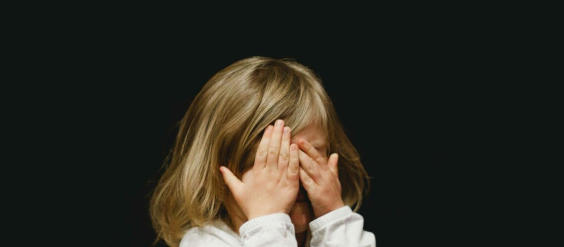 A little girl covering her face with her hands.