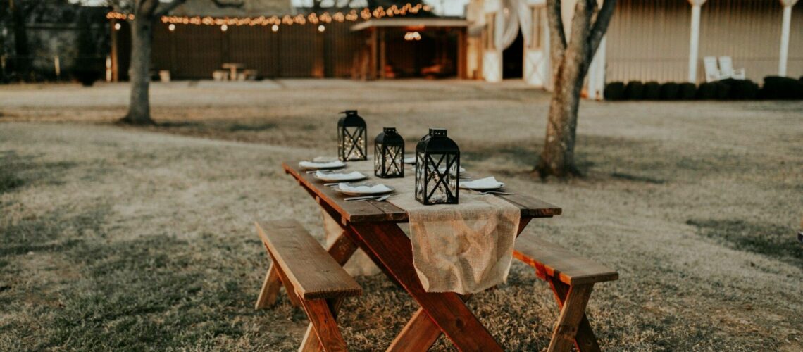 A picnic table set up in a field with lanterns.