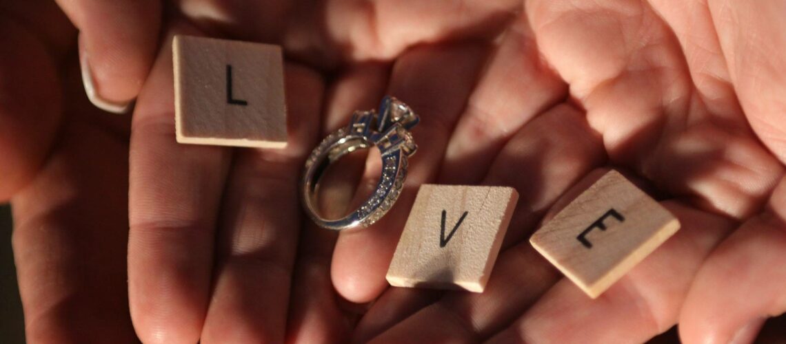 Two hands holding a wedding ring and scrabble letters.