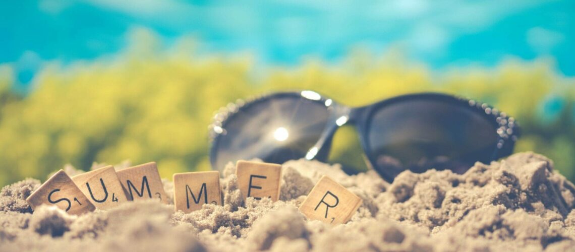 Sunglasses and the word summer spelled out in the sand.