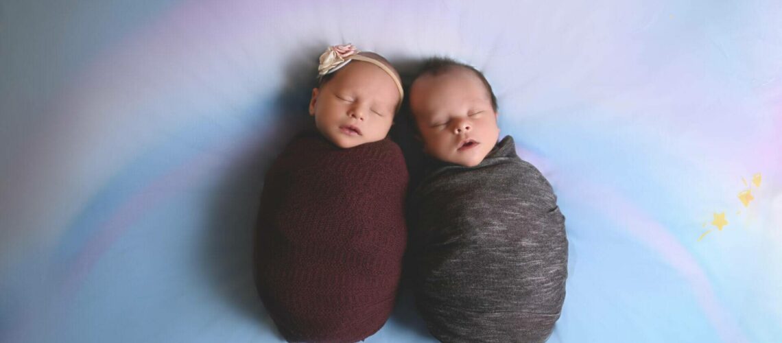 twin newborns wrapped laying on a rainbow background, newborn photography