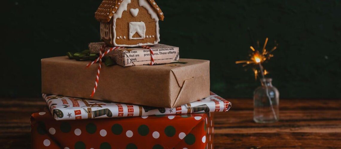 A stack of christmas presents with a gingerbread house on top.