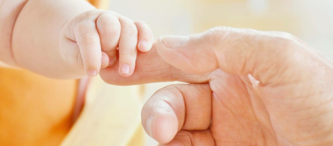A baby's hand is being held by an older man.