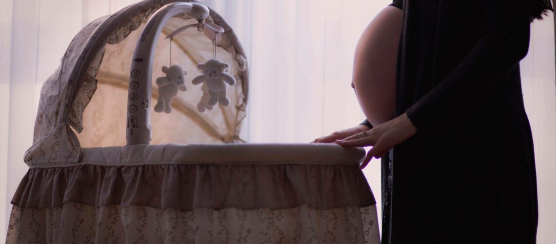A pregnant woman standing next to a cradle.