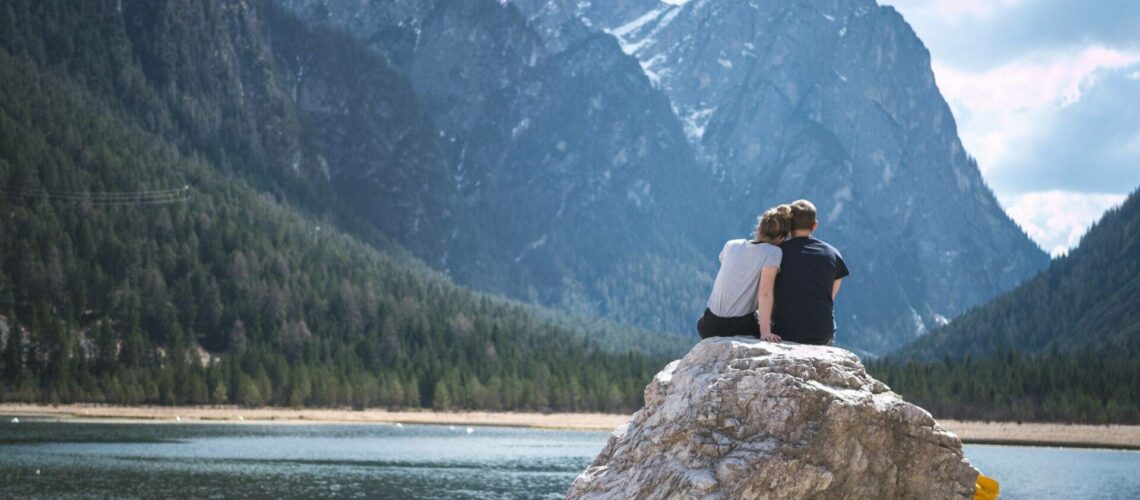 A couple sitting on a rock overlooking a lake.