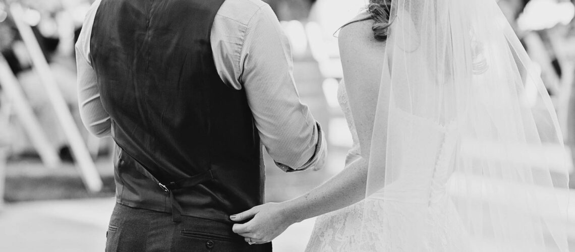 Black and white photo of a bride and groom holding hands.