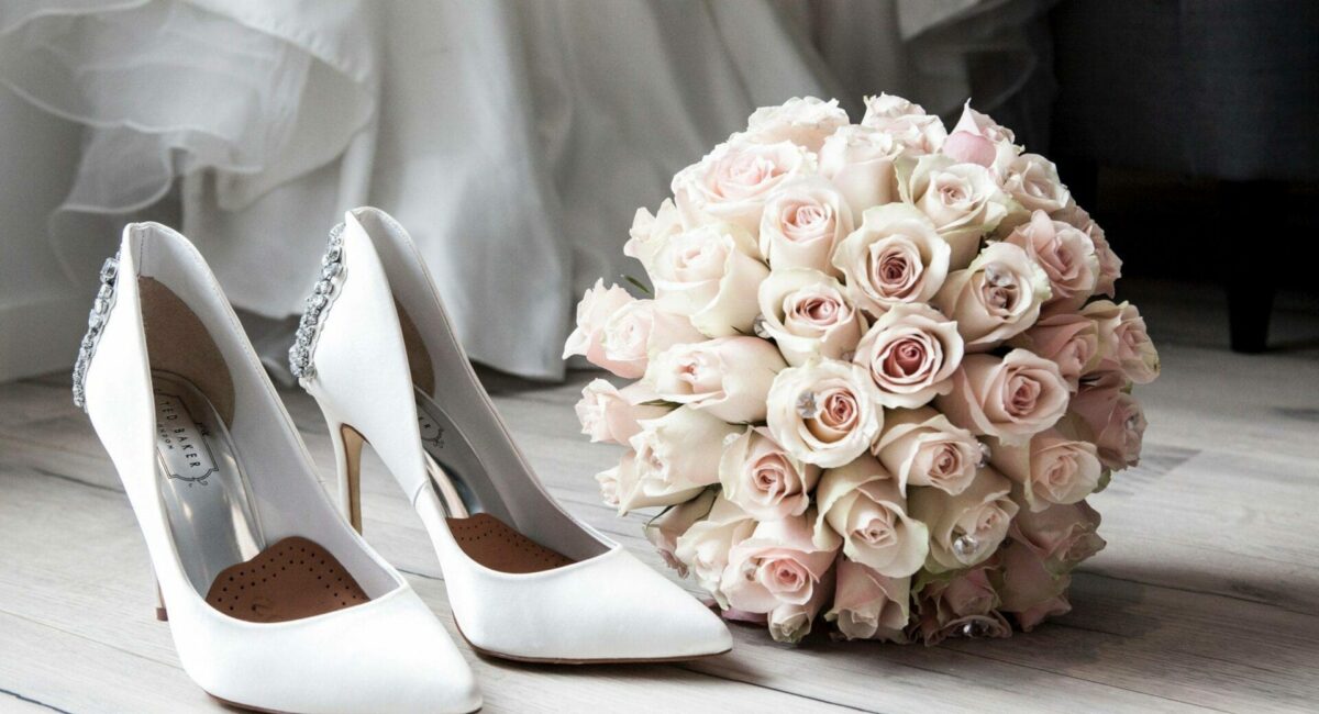 A bouquet of roses and wedding shoes on a wooden floor.