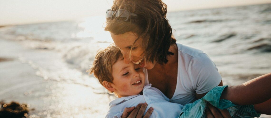 A mother holding her son on the beach.